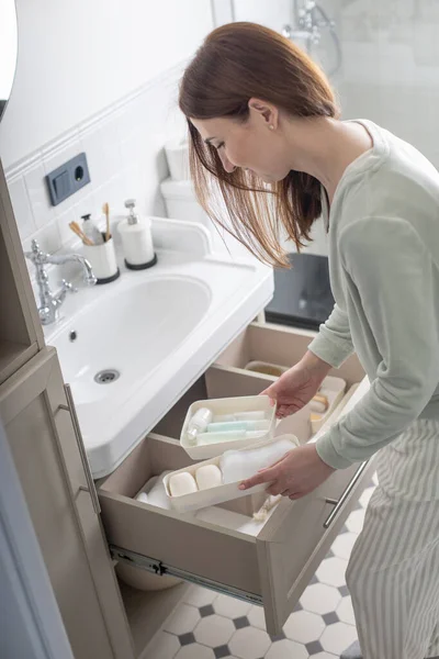 Ev hanımı elleri havluyu lavabonun altındaki açık çekmeceye koyuyor. Banyo manzarasında depolama alanı düzenleyen bir kadın. Kadın evde temizlik yapıyor. Modern Marie Kondo 'nun metodu