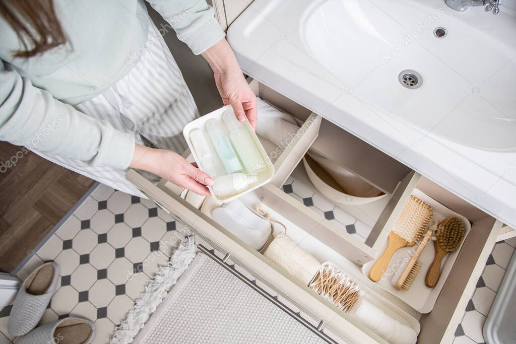 Housewife hands putting rolled up towel into open drawer under sink. Female organizing storage space in bathroom top view. Woman cleaning housework at home. Modern Marie Kondo's keeping method