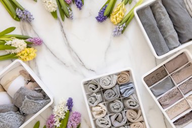 Mari Kondo 'nun doğal çiçeklerle süslenmiş iç çamaşırı organizasyonu. Üst görünüm çağdaş katlanmış konteynır kılıfları mermer zeminde giysi. Güzel gardırop.