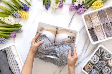 Mari Kondo 'nun doğal çiçeklerle süslenmiş iç çamaşırı organizasyonu. Üst görünüm çağdaş katlanmış konteynır kılıfları mermer zeminde giysi. Güzel gardırop.