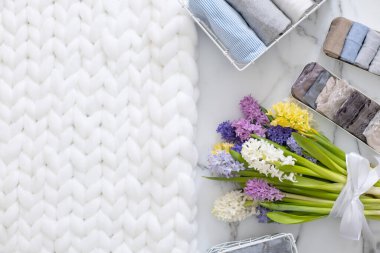 Mari Kondo 'nun doğal çiçeklerle süslenmiş iç çamaşırı organizasyonu. Üst görünüm çağdaş katlanmış konteynır kılıfları mermer zeminde giysi. Beyaz pofuduk ekose örgü.