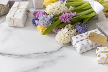 Çiçeklerle süslenmiş, kutuya sarılı kurdeleli, son moda kompozisyon. Beyaz mermer üzerinde doğal çiçeklerle süslenmiş şık hediyeler. Güzel bayram kutlaması