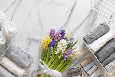 Mari Kondo 'nun doğal çiçeklerle süslenmiş iç çamaşırı organizasyonu. Üst görünüm çağdaş katlanmış konteynır kılıfları mermer zeminde giysi. Beyaz metal kablo sepetleri.