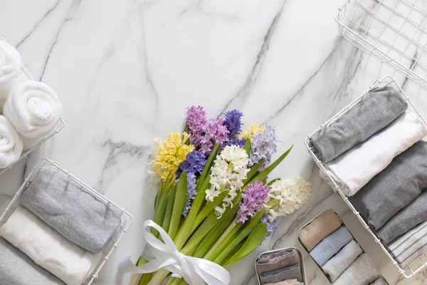 Mari Kondo 'nun doğal çiçeklerle süslenmiş iç çamaşırı organizasyonu. Üst görünüm çağdaş katlanmış konteynır kılıfları mermer zeminde giysi. Beyaz metal kablo sepetleri.