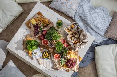 Üst kattaki konforlu oda servis masasının etrafı rahat yastıklarla çevrili ve parti kutlaması için hazır. Sağlıklı, taze, lezzetli yemek ve içecek rahat oturma odası hygge boho scandi dekoru.