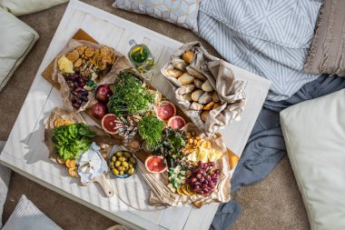 Üst kattaki konforlu oda servis masasının etrafı rahat yastıklarla çevrili ve parti kutlaması için hazır. Sağlıklı, taze, lezzetli yemek ve içecek rahat oturma odası hygge boho scandi dekoru.
