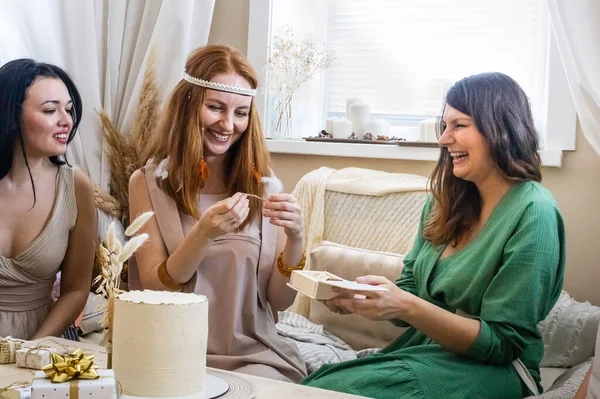 Adorable rejoicing redhead woman taking wrapped gift box celebrating birthday in modern hippie bohemian style. Happy female receiving present from friends having positive emotion at hen-party