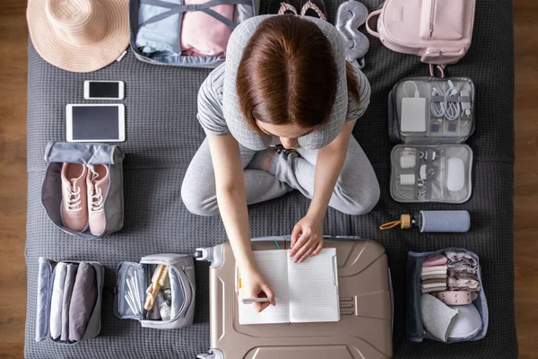 Glimlachende toeristische vrouw verpakking koffer naar vakantie schrijven papieren lijst klaar om te reizen — Stockfoto