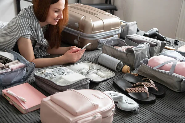 Vrouw chatten surfen internet gebruik smartphone applicatie tijdens het verpakken koffer bagage — Stockfoto