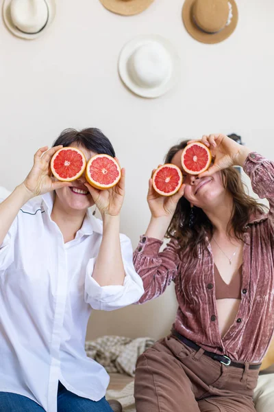 Amigos femininos felizes mostrando línguas posando com metades de toranjas nos olhos rindo da festa das galinhas — Fotografia de Stock