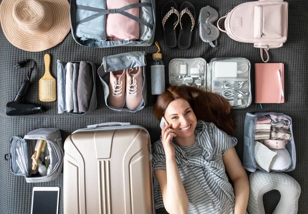 Divertida mujer de viaje acostada en la cama hablando teléfono inteligente cansado embalaje cosas para viajar viaje vacaciones — Foto de Stock