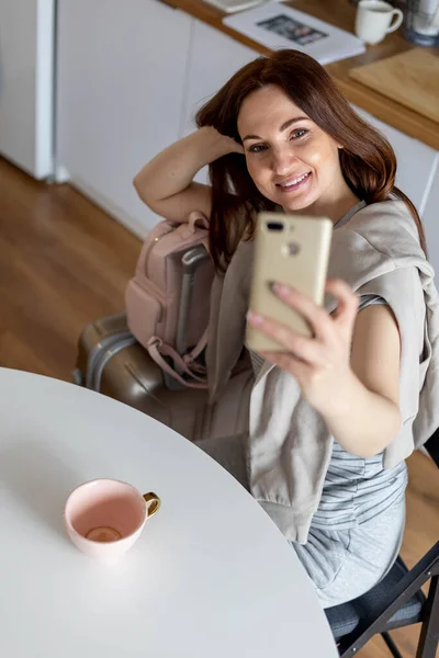 Mulher sorridente posando na cozinha tirando selfie com bagagem viagem de verão férias na cozinha — Fotografia de Stock