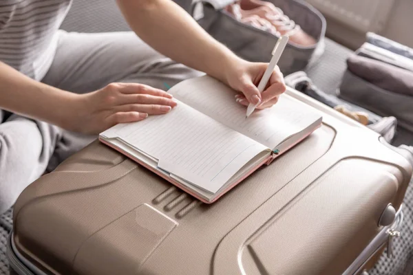 Primeros planos manos femeninas escribir notas en papel haciendo lista de cosas necesarias para viajar de vacaciones — Foto de Stock