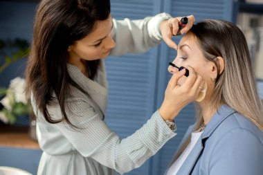 Makyaj sanatçısı, güzellik salonunda çalışan makyaj fırçasına makyaj malzemesi uyguluyor.