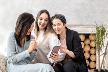 Grup mutlu bayan arkadaşlar internette sohbet ediyorlar. Akıllı telefon kullanıyorlar. Gülümsüyorlar.