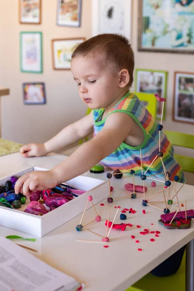 一个小男孩在家里的桌子上从塑料中雕刻出来。做了一个牙签和球的塔. — 图库照片