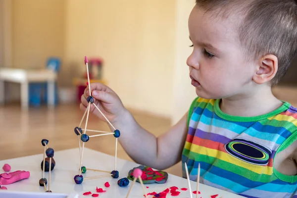 一个小男孩在家里的桌子上从塑料中雕刻出来。做了一个牙签和球的塔. — 图库照片