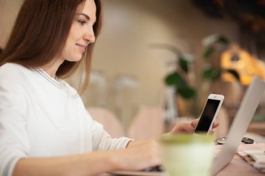 Genç bir kadın dizüstü bilgisayarda günlük program hazırlıyor ve kafede kahve molası veriyor..