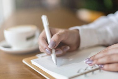 Kapalı kadın elleri not defterine kağıt notlar yazarken kalem masası kafeteryasında günlük yazarken, planlarken.