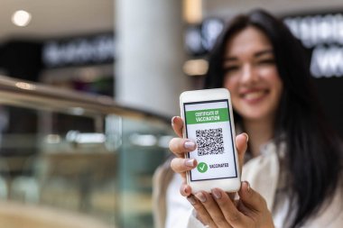 Aşı sertifikasıyla akıllı telefon ekranında poz veren gülümseyen kadın. Coronavirus önleme