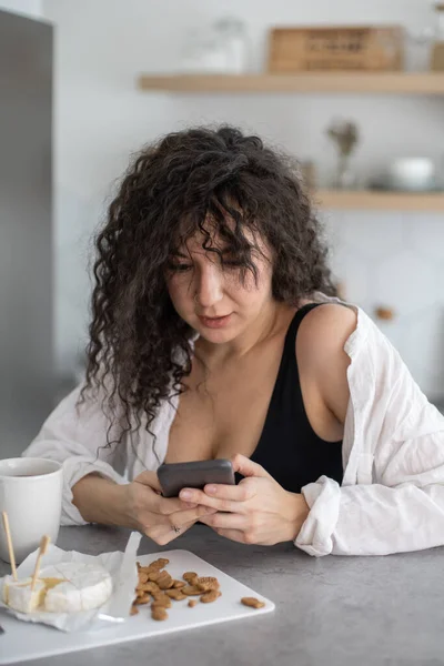 Fröhliche brünette Frau im Chat surft mit Smartphone und genießt Kaffeepause im Café — Stockfoto