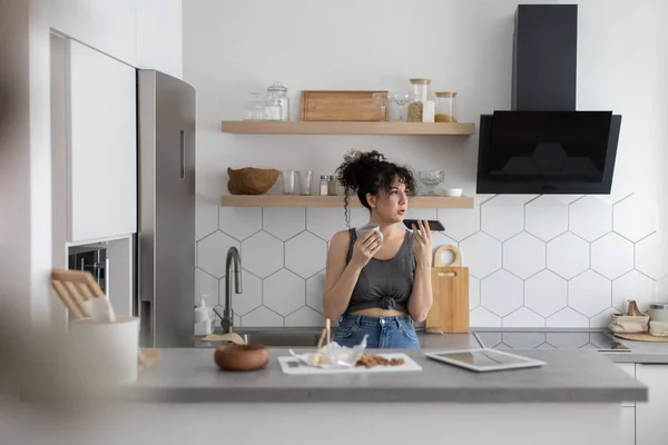 現代のキッチンでリラックスした快適な国内の女性チャットはスマートフォンの白い料理を使用インテリア — ストック写真