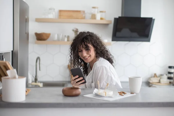 Junge Hausfrauen schreiben SMS und kommunizieren soziale Netzwerke in der weißen nordischen Küche — Stockfoto