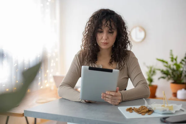 Smiling modern brunette woman surfing internet use tablet sitting at table in minimalistic interior — 图库照片