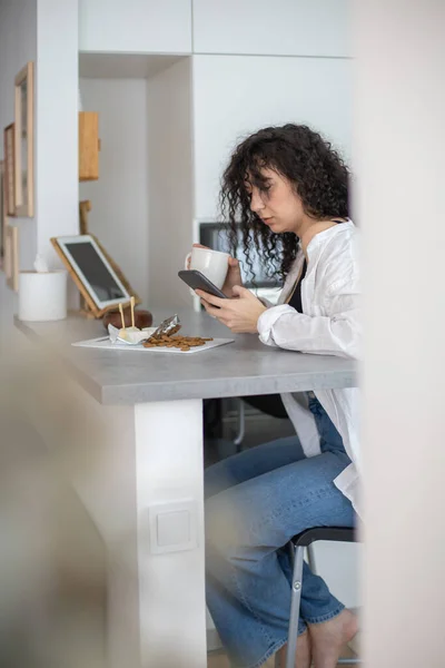 Los mensajes de texto de mensajes de texto femeninos domésticos jóvenes comunican redes sociales en la cocina nórdica blanca —  Fotos de Stock