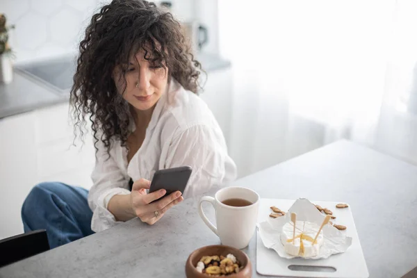 Junge Hausfrauen schreiben SMS und kommunizieren soziale Netzwerke in der weißen nordischen Küche — Stockfoto