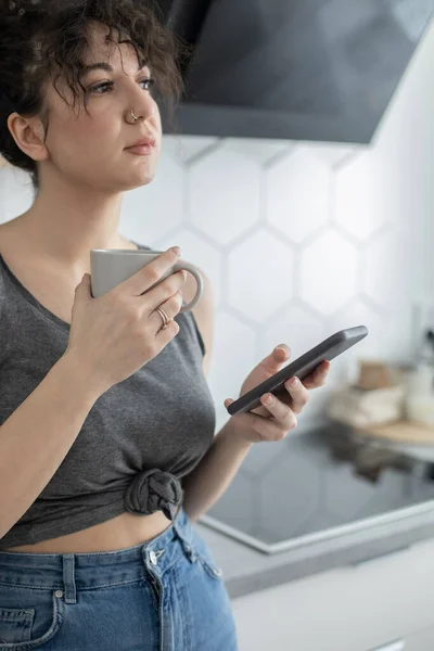 Fröhliche brünette Frau im Chat surft mit Smartphone und genießt Kaffeepause im Café — Stockfoto