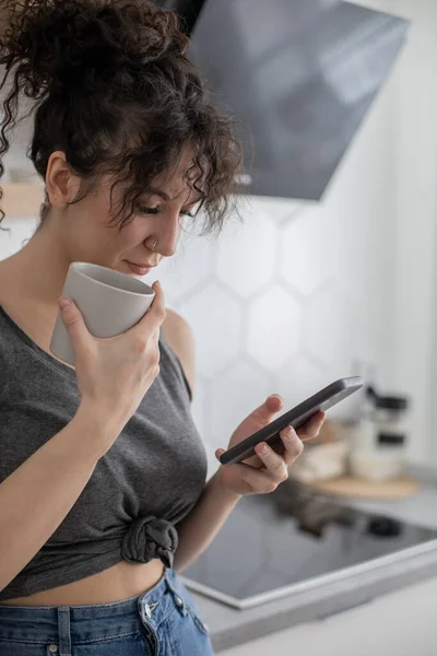 Fröhliche brünette Frau im Chat surft mit Smartphone und genießt Kaffeepause im Café — Stockfoto