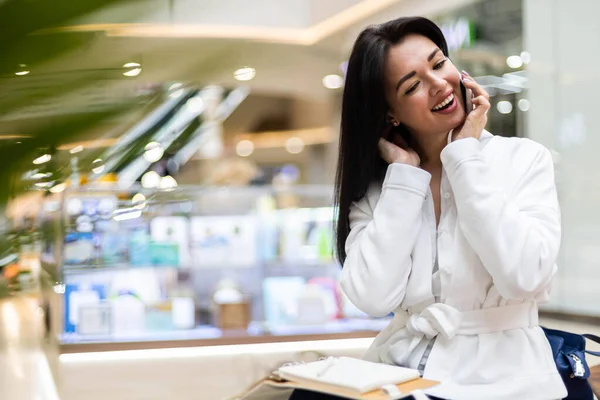 쾌활 한 사업가가 현대 쇼핑몰에서 긍정적 인 감정을 가지고 스마트폰으로 웃으며 말하는 모습 — 스톡 사진