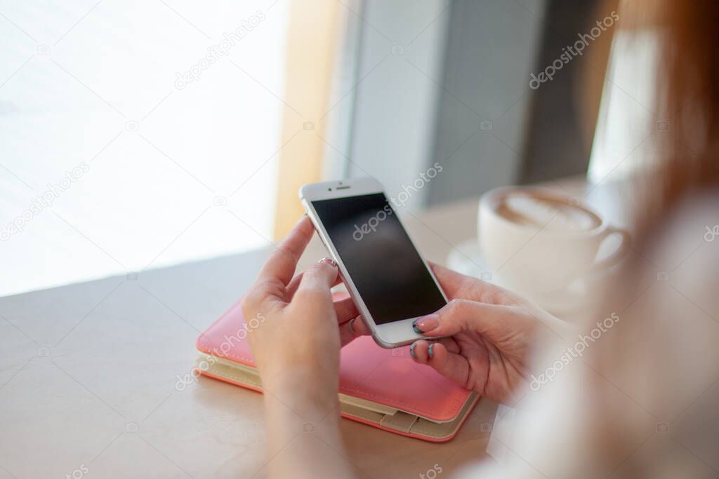 Female hands using mobile phone for organising schedule while drinking latte during the coffee break