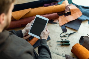 Üst düzey erkek tabakçı deri atölyesinde tablet kullanıyor. Sanatçı çevrimiçi reklam promosyonu yapıyor