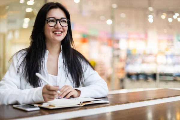 Felice Asiatica giovane donna seduta al caffè con tazza di caffè prendere appunti godendo di pausa — Foto Stock