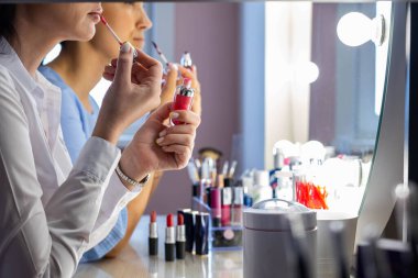 Kapanış makyajı sanatçısı, kadın müşteriye ders sırasında dudak parlatıcısı sürmesini öğretiyor.