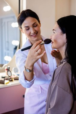 Güzellik salonunda çalışan kadın müşteriye kozmetik dudak kalemi süren mutlu bir makyöz.