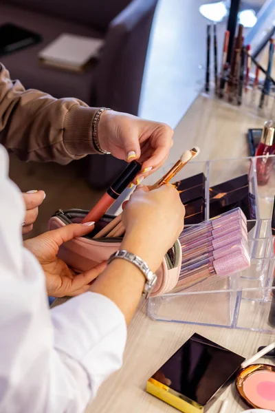 Artista de maquillaje femenino analizando bolsa cosmética del cliente. Enseñanza de elegir cepillos y brillo de labios — Foto de Stock