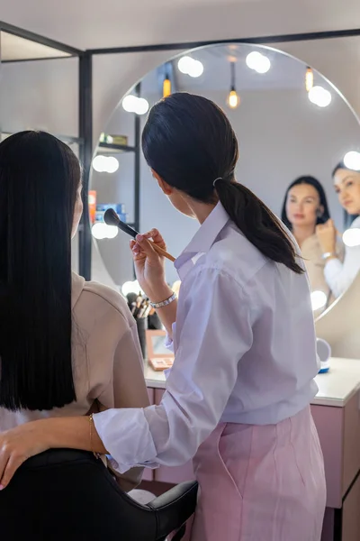 マスタークラスで顔の使用ブラシに赤面を適用する女性クライアントを教えるプロの化粧アーティスト — ストック写真
