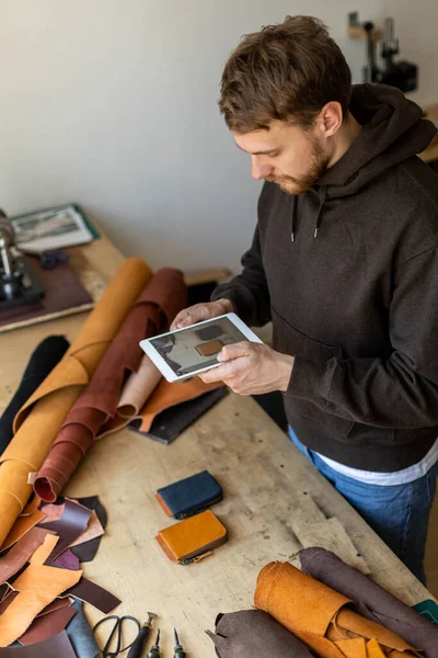 Üst düzey erkek tabakçı deri atölyesinde tablet kullanıyor. Sanatçı çevrimiçi reklam promosyonu yapıyor — Stok fotoğraf