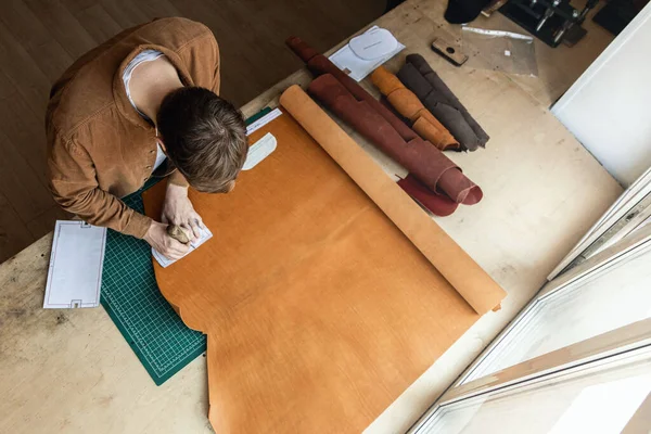 Male tanner making cutting scheme of bag working at leather workshop. Handcrafted creating — Stock Photo, Image