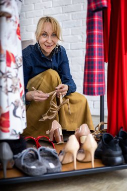 Gülümseyen sarışın kadın moda stüdyosunda ya da butikte ayakkabı seçerken alışverişin keyfini çıkarıyor.