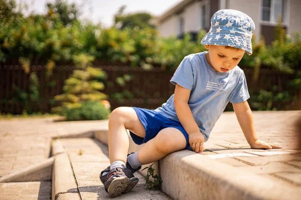 Веселий маленький хлопчик малює ковдра з крейдою на землі, насолоджуючись щасливим дитинством на задньому дворі — стокове фото