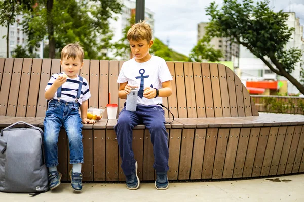 Fröhliche kleine Brüder spazieren auf kindlichem Sportplatz und essen entspannt frisches Obst — Stockfoto