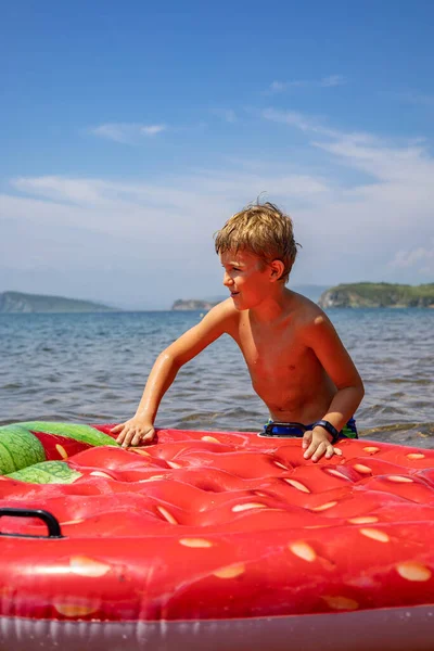 Neşeli erkek çocuk deniz suyuyla çevrili şişirilebilir çilek cankurtaran şamandırasında yüzüyor. — Stok fotoğraf