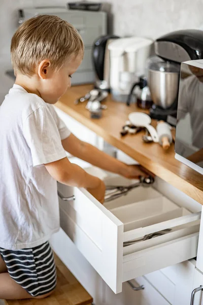 The boy helps his mother in the kitchen to put things in order. Places forks, spoons and cutlery in place. — Stock Photo, Image