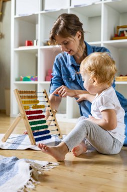 Anne, küçük çocuğa yerde çok renkli ahşap ekolojik abaküslere güvenmeyi öğretiyor.