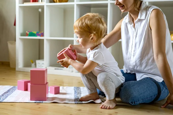 年轻的母亲和小宝宝组装粉红立方体Maria Montessori生态材料 — 图库照片