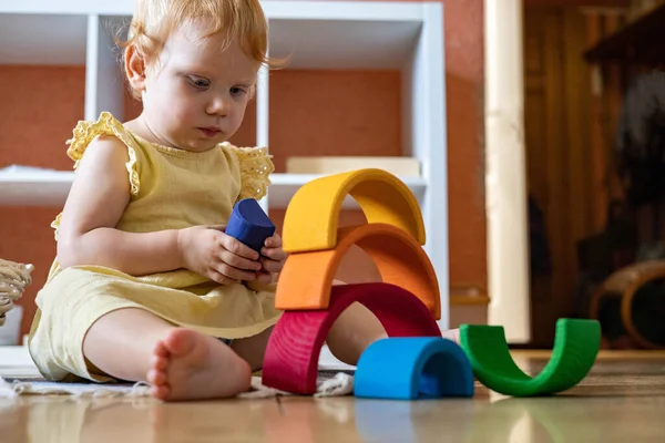 Bebé niña en vestido apilamiento arco iris bloque construcción edificio ecológico madera juguete torre — Foto de Stock